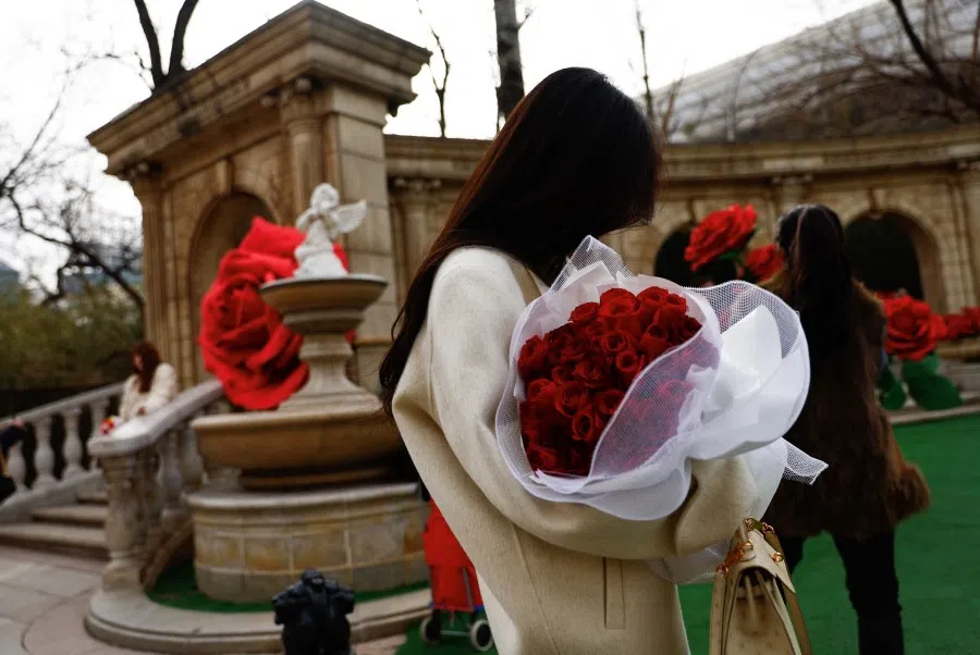 A woman holds a rose bouquet in front of giant rose installations on Valentine's Day in Beijing, China, 14 February 2023. (Tingshu Wang/Reuters)
