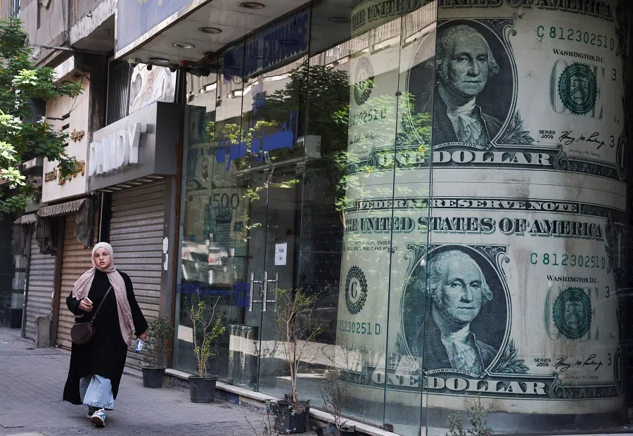 An Egyptian woman walks past a currency exchange point, displaying images of the US dollar, in Cairo, Egypt, on 9 May 2024. (Amr Abdallah Dalsh/Reuters)