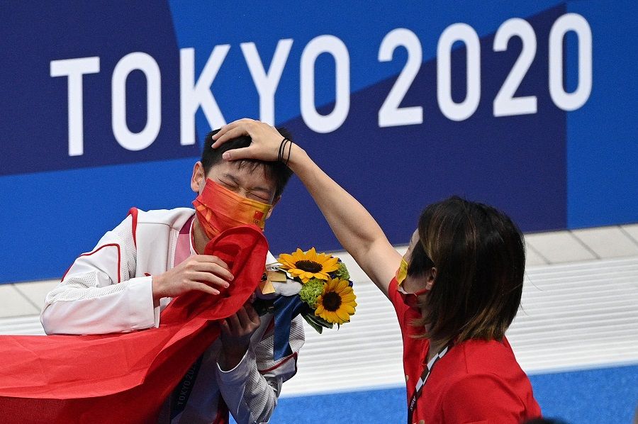 Gold medalist Quan Hongchan has her hair ruffled by a member of the coaching staff as she leaves the pool after winning the women's 10m platform diving final event during the Tokyo 2020 Olympic Games at the Tokyo Aquatics Centre in Tokyo, Japan, on 5 August 2021. (Oli Scarff/AFP)
