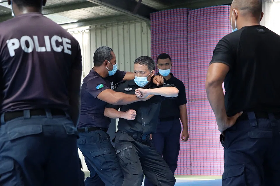 An undated handout photo released on 29 March 2022 by the Royal Solomon Islands Police Force (RSIPF) shows a China Police Liason Team officer (centre) training local RSIPF officers. (Handout/RSIPF/AFP)