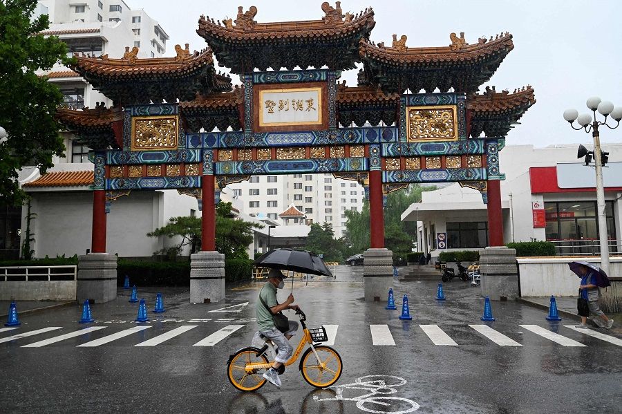 A man rides a bike while sheltering from the rain in Beijing, China, on 31 July 2023. (Pedro Pardo/AFP)