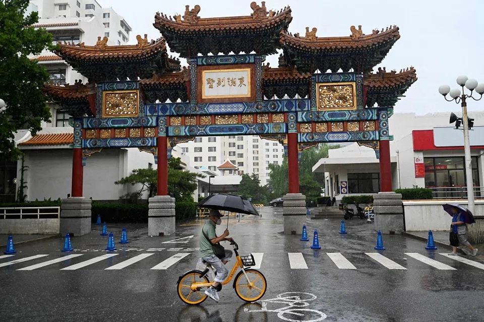 A man rides a bike while sheltering from the rain in Beijing, China, on 31 July 2023. (Pedro Pardo/AFP)