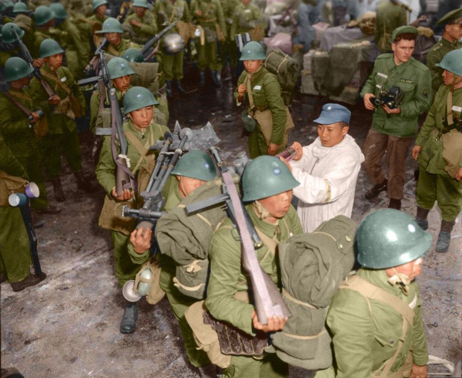 KMT troops standing at attention in full uniform as they arrive in Keelung from Dachen, February 1955. Health officials are using spray dispensers to decontaminate their clothes and bags.