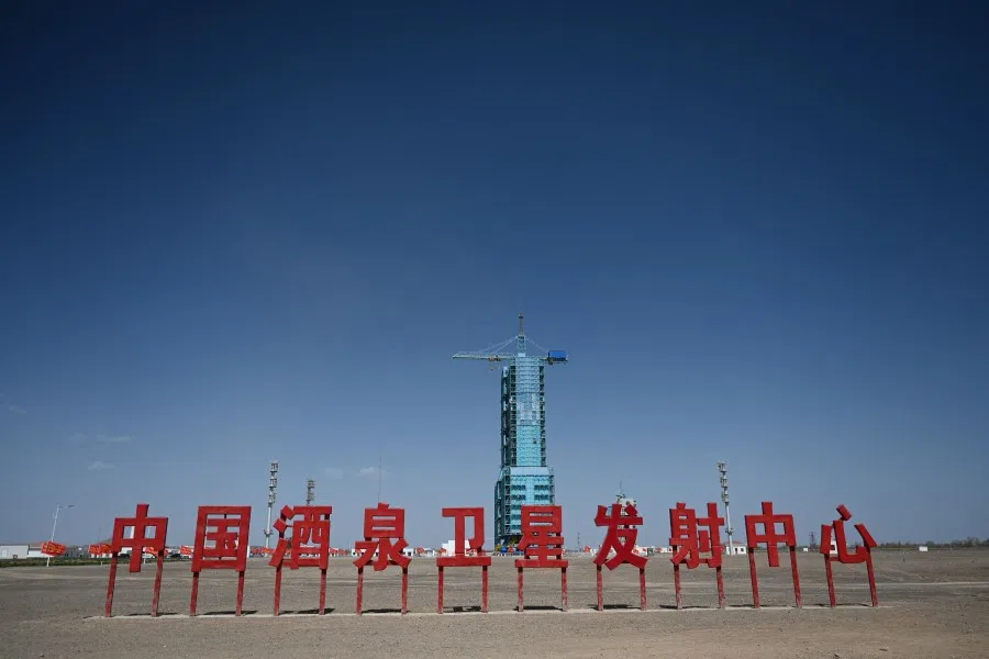 A Long March-2F carrier rocket, carrying the Shenzhou-18 spacecraft, is seen encased in a shield on the launch pad, behind a sign which reads “China Jiuquan Satellite Launch Center”, a day before the launch of the mission, at the Jiuquan Satellite Launch Centre in the Gobi desert in northwest China on 24 April 2024. (Greg Baker/AFP)