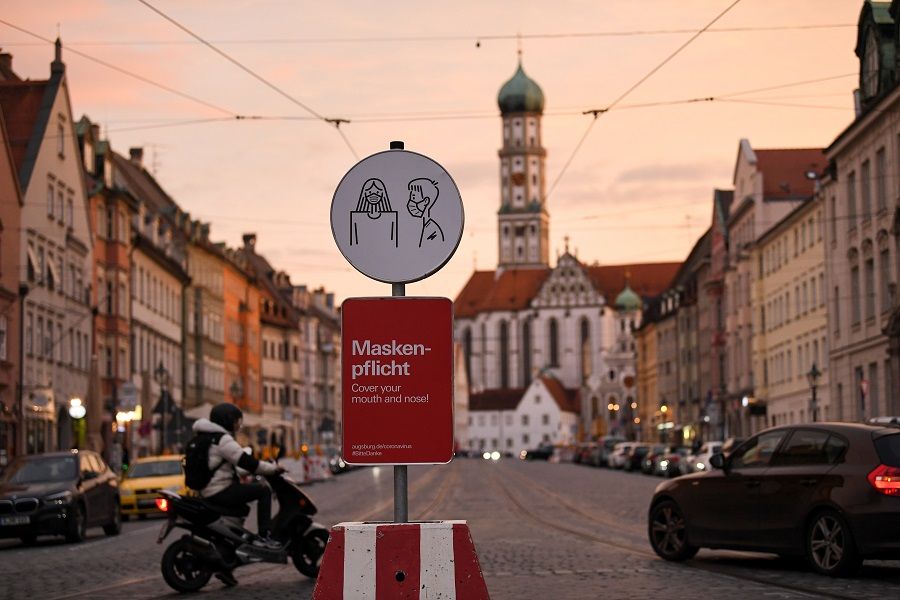 A person drives a motorcycle on a street near a sign that reminds people how to wear a face mask correctly, in Augsburg, Germany, 30 October 2020. (Andreas Gebert/Reuters)