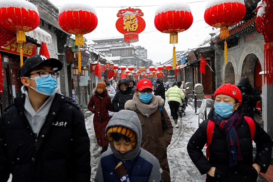 People walk at a hutong alley decorated with lanterns on a snowy day in Beijing, China, 13 February 2022. (Tingshu Wang/Reuters)