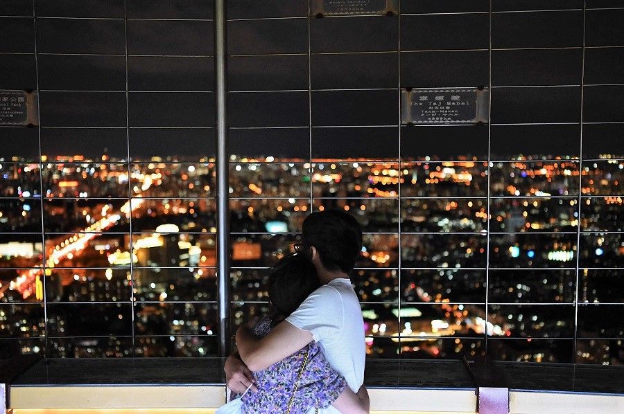 A couple hug as they look out at a night view through a fence at the Central Television Tower in Beijing, China, on 26 August 2021. (Jade Gao/AFP)