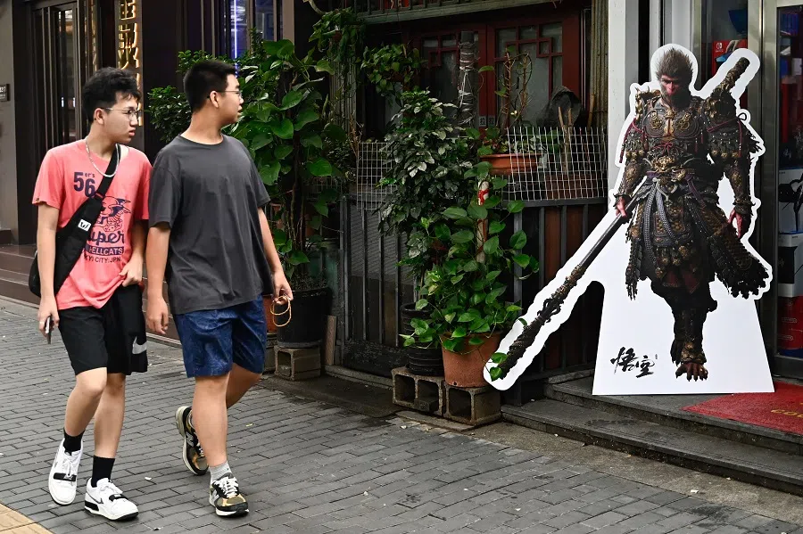 Two young people walk past a cardboard cutout of the Monkey King character of the Chinese action role-playing game Black Myth: Wukong during its launch day in Beijing, China, on 20 August 2024. (Pedro Pardo/AFP)