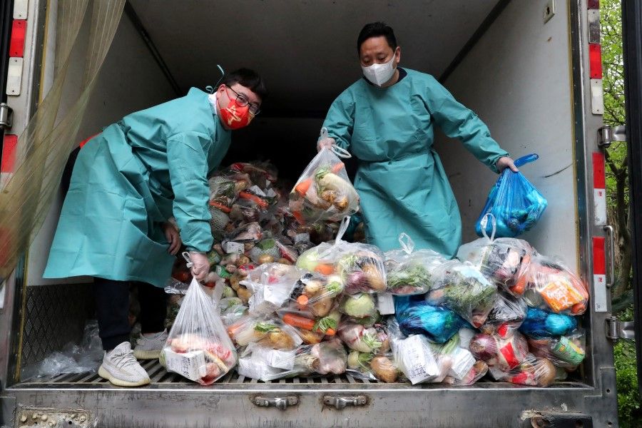 Workers wearing protective gear sort bags of vegetables and groceries on a truck to distribute them to residents at a residential compound, during the lockdown to curb the coronavirus disease (Covid-19) outbreak in Shanghai, China, 5 April 2022. (China Daily via Reuters)