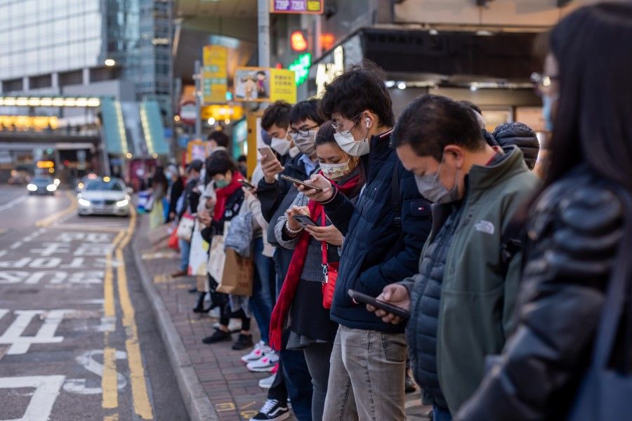 Commuters look at smartphones at a bus stop in Hong Kong, China, on 4 February 2022. (Paul Yeung/Bloomberg)