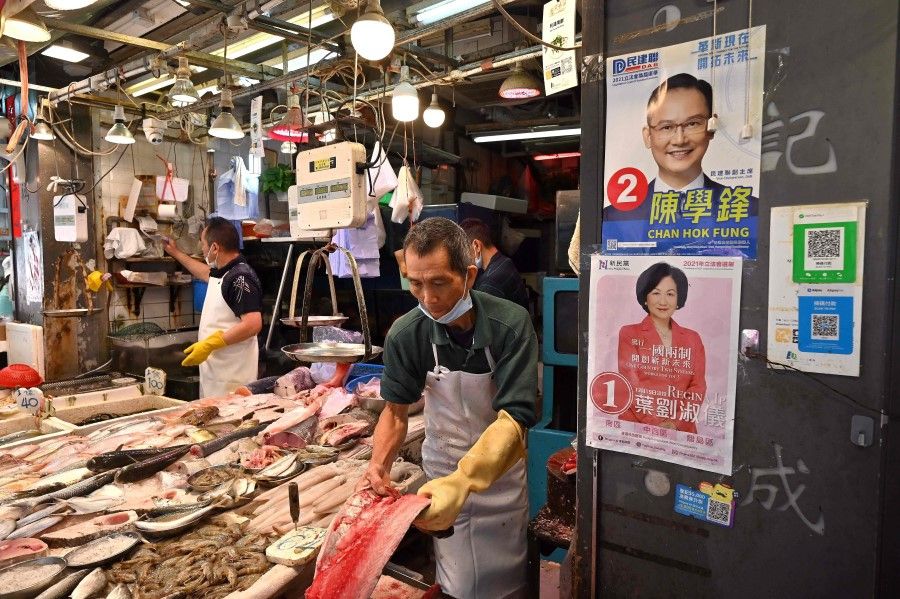 Fishmongers work next to campaign posters on the wall at a market in Hong Kong on 8 December 2021, ahead of the city's legislative elections on 19 December. (Peter Parks/AFP)