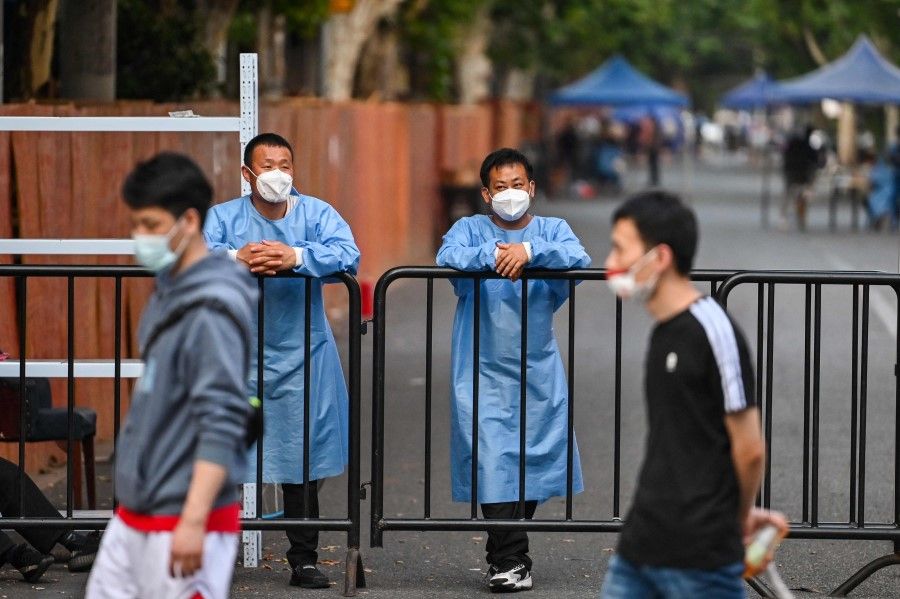 Workers wearing protective gear stand behind a fence blocking a street in a residential area under a Covid-19 lockdown in the Huangpu district of Shanghai on 16 June 2022. (Hector Retamal/AFP)