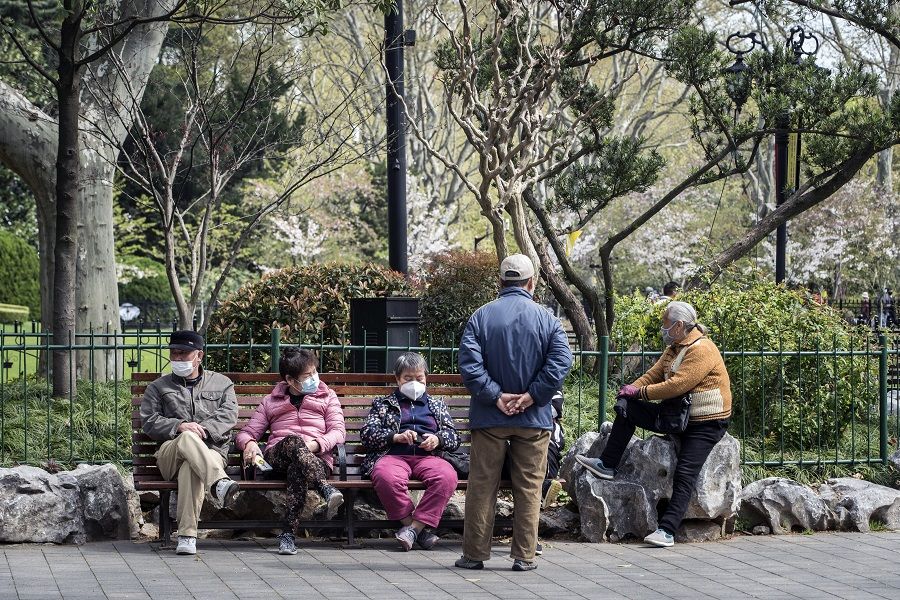 People wearing protective masks sit on a bench at Lu Xun Park in Shanghai, China, on 2 April 2020. (Qilai Shen/Bloomberg)