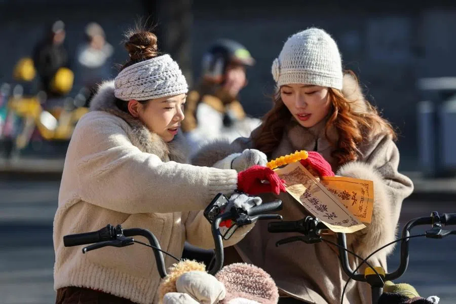 Two Chinese women buy sweet candy sticks from a street vendor in Beijing on 2 December 2025. (Ludovic Marin/AFP)