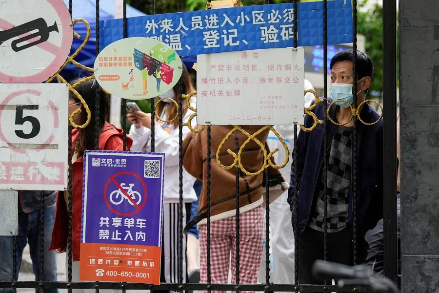 A resident waiting for a food delivery looks out from behind a gate blocking an entrance to a residential area under lockdown amid the Covid-19 pandemic, in Shanghai, China, 13 April 2022. (Aly Song/Reuters)