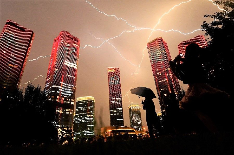 A bolt of lightning crosses the sky as people look at buildings displaying a light show on the eve of the 100th anniversary of the Chinese Communist Party in Beijing, China, on 30 June 2021. (Noel Celis/AFP)