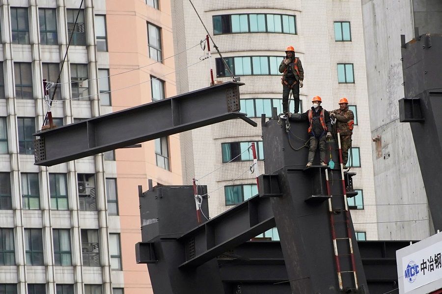 Workers watch as a crane lifts a structure at a construction site in Shanghai, China, 14 January 2022. (Aly Song/Reuters)