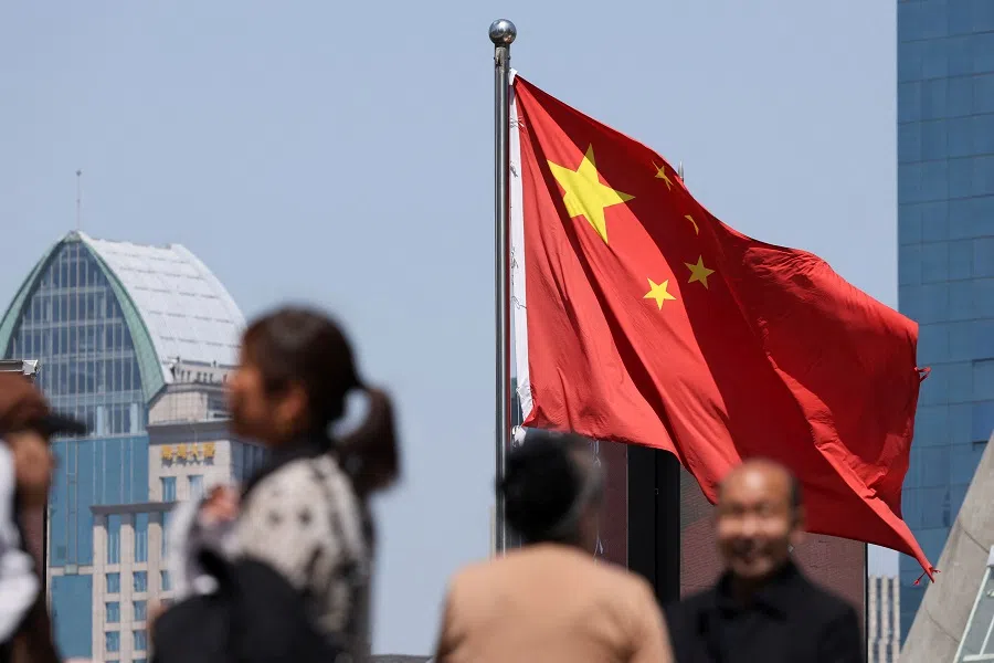 A Chinese national flag flies as people walk on a pedestrian bridge at the Lujiazui financial district in Shanghai, China, on 15 April 2025.