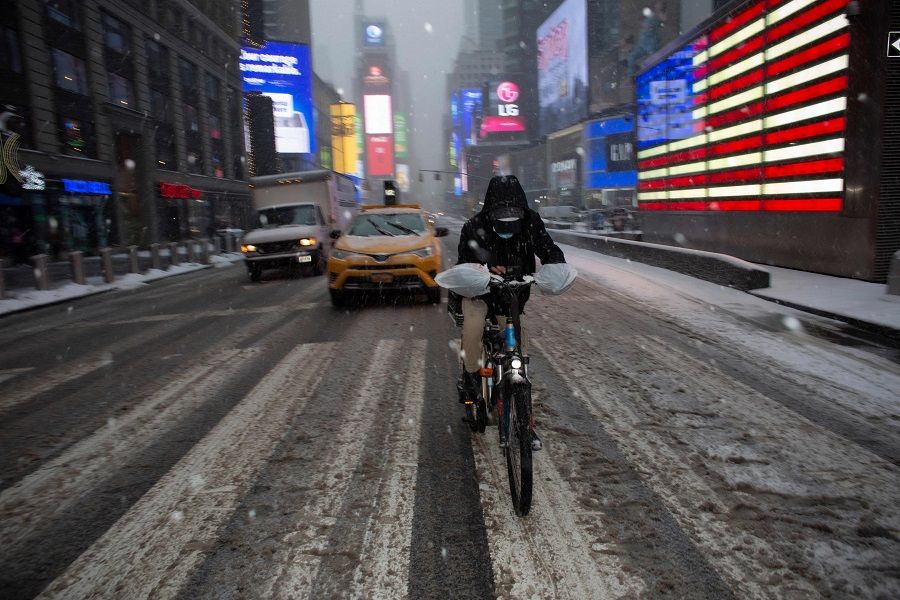 A man rides a bicycle as snow falls in New York's Times Square on 18 February 2021.(Kena Betancur/AFP)