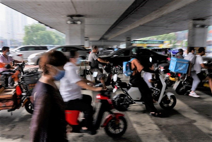 People ride on scooters across a street during morning rush hour, in Beijing, China, 2 August 2022. (Tingshu Wang/Reuters)