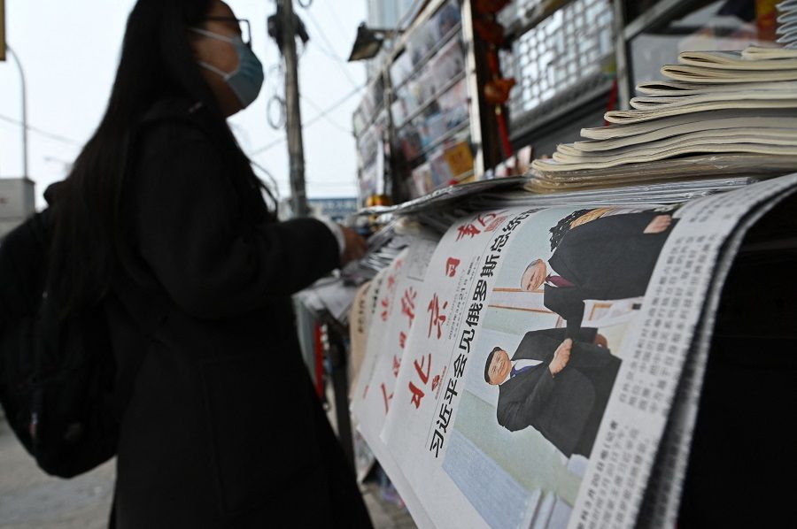A woman waits next to newspapers featuring a front page photo of Chinese President Xi Jinping meeting with Russian President Vladimir Putin in Moscow, at a news stand in Beijing, China, on 21 March 2023. (Greg Baker/AFP)