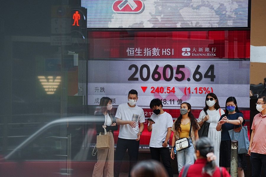 People walk past a screen displaying the Hang Seng Index at Central district, in Hong Kong, 19 July 2022. (Lam Yik/Reuters)