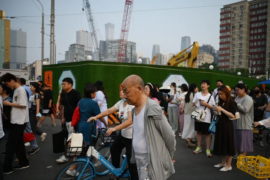 People wait to cross a road near a construction site in Beijing, China, on 9 July 2024.