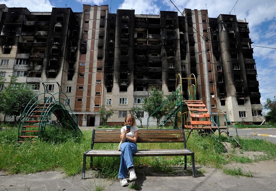 In this file photo taken on 16 June 2022, a girl looks at her smartphone as she sits on a bench in front of residential buildings partially destroyed as a result of the shelling in town of Irpin, near the Ukrainian capital of Kyiv. (Sergei Chuzavkov/AFP)