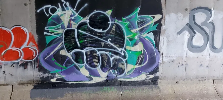 Figure 4: Vandalism on graffito. The graffito by a team “Karoshi” vandalised by another team “AK”, stylised in the car-like tag. Karoshi had accidentally covered a small corner of an AK graffito elsewhere, violating #3. This led to rather over-the-top retaliation by AK against all Karoshi’s works throughout Hong Kong. AK’s approach violates #2 by vandalising a piece with a tag. Karoshi chose to disengage.