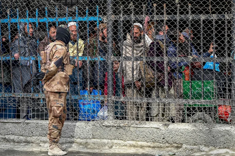 In this photograph taken on 2 February 2023, a Taliban security personnel speaks with Afghan people waiting behind a fenced corridor before they cross into Pakistan at the zero point Torkham border crossing between Afghanistan and Pakistan, in Nangarhar province. (Wakil Kohsar/AFP)