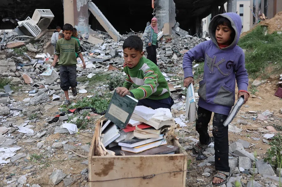 Displaced Palestinians collect books from the destroyed Islamic University to use as fuel to cook food, in Gaza City on 21 March 2025.
