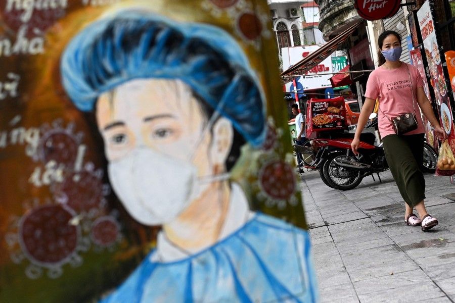 A woman wearing a T-shirt that reads, "Everything will be fine" walks past an electricity box decorated with a Covid-19 coronavirus-themed painting along a street in Hanoi on 8 July 2021. (Manan Vatsyayana/AFP)