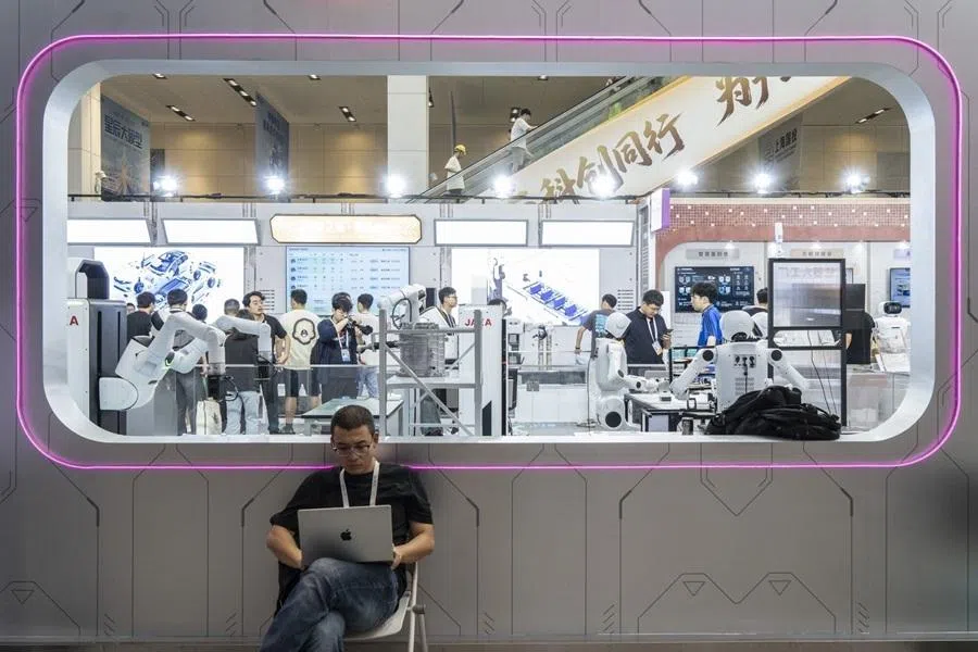 A man works on his computer in front of a display area for robots demonstrating various industrial applications during a media preview of the WAIC in Shanghai, China, on 16 July 2026.