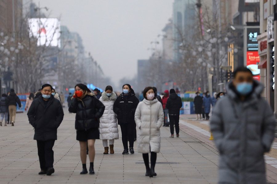 People walk at a shopping street in Beijing, China, 24 January 2022. (Tingshu Wang/Reuters)