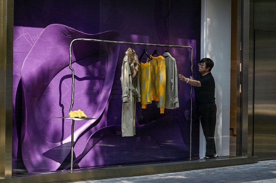 A salesperson checks clothes displayed in a shopfront window at a mall in Beijing, China, on 15 September 2023. (Jade Gao/AFP)
