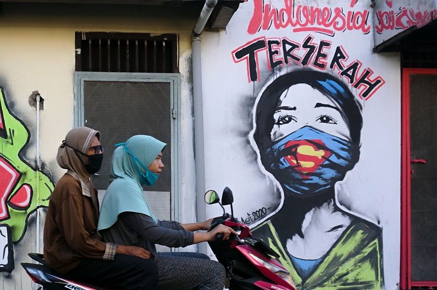 Two girls wearing face masks ride a scooter past a mural reading "whatever Indonesia" in Tangerang on 23 May 2020. (Fajrin Raharjo/AFP)
