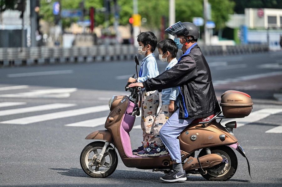 A man rides a scooter with two children on board during a Covid-19 lockdown in the Jing'an district of Shanghai, China, on 25 May 2022. (Hector Retamal/AFP)