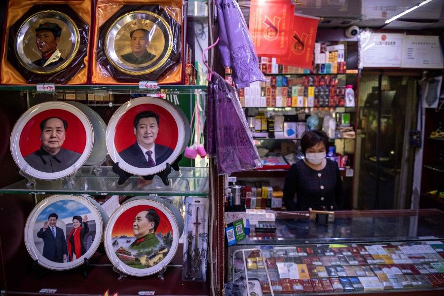 A vendor (R) at a souvenir shop stands next to plates on display with the picture of Chinese President Xi Jinping and the late Communist Party leader Mao Zedong (L, centre) in Beijing, 19 May 2020. (Nicolas Asfouri/AFP)