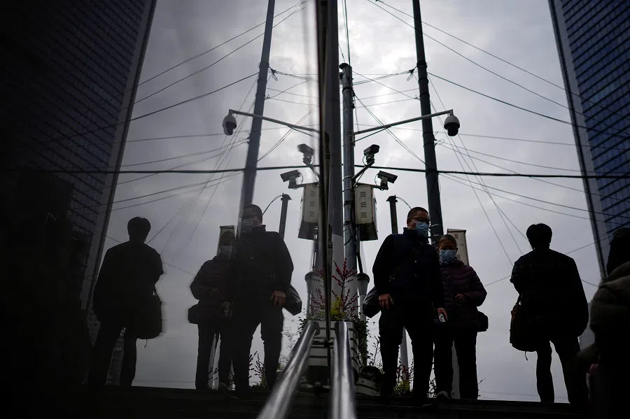People wearing face masks walk under surveillance cameras on a street in Shanghai, China, 12 December 2022. (Aly Song/Reuters)