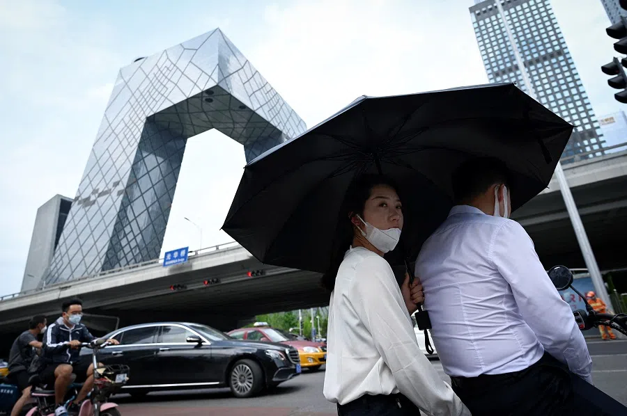 A couple riding an electric bicycle waits to cross a street at the central business district in Beijing, China, on 8 July 2022. (Wang Zhao/AFP)