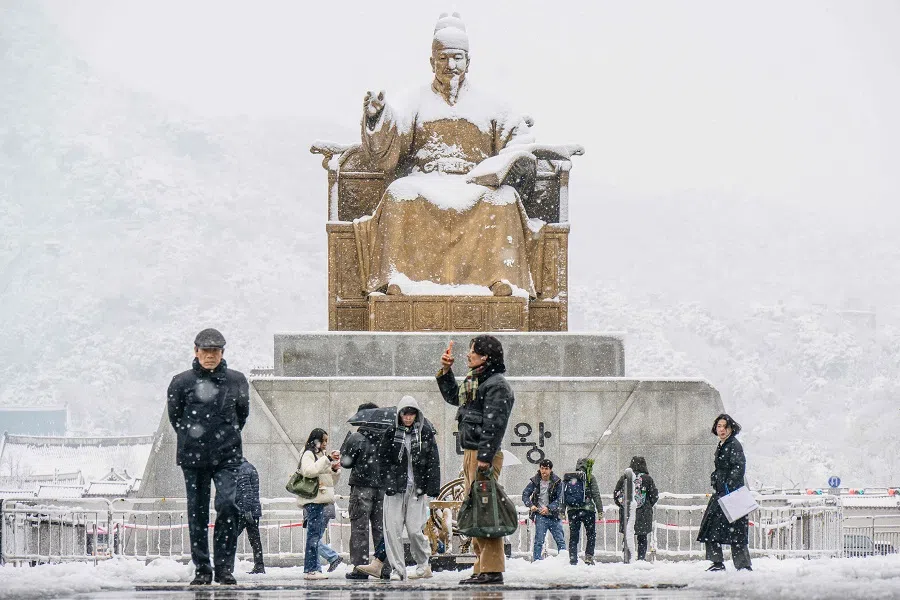 People walk in front of the Statue of King Sejong the Great, dedicated to the 15th century Korean monarch, in Gwanghwamun Square amid heavy snowfall in central Seoul on 27 November 2024.