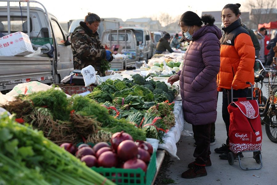 A woman looks at vegetables displayed at a stall at an outdoor market in Beijing, China, on 12 January 2024. (Florence Lo/Reuters)