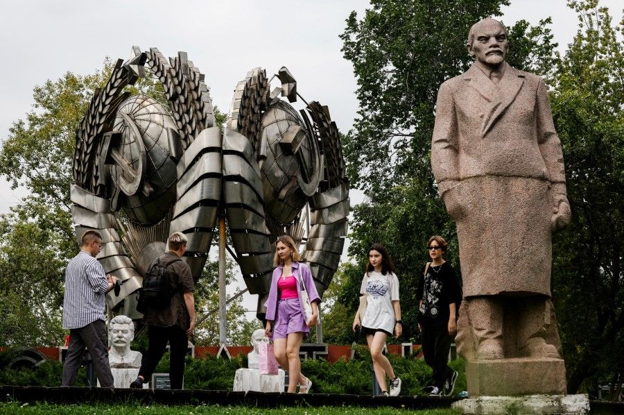 People walk past a monument to Soviet state founder Vladimir Lenin and a coat of arms of the Soviet Union in a park in Moscow, Russia, 8 August 2023. (Maxim Shemetov/Reuters)
