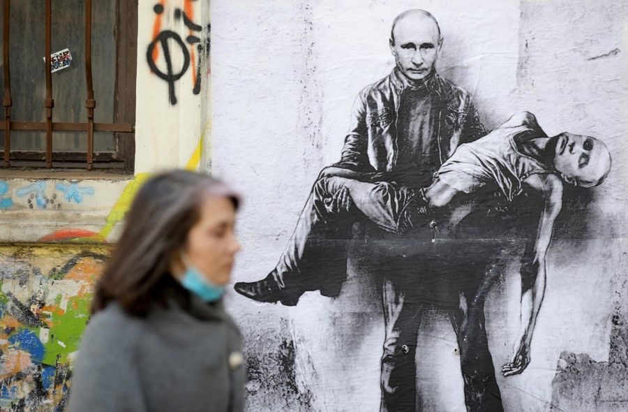 A woman walks past a poster depicting Russian President Vladimir Putin holding his own body, as Russia's invasion of Ukraine continues, in Sofia, Bulgaria, 28 March 2022. (Spasiyana Sergieva/Reuters)