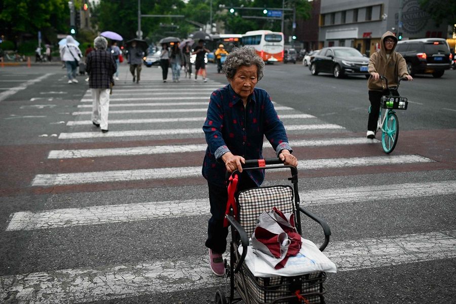 An elderly woman pushing a cart crosses a street in Beijing, China, on 12 May 2023. (Wang Zhao/AFP)