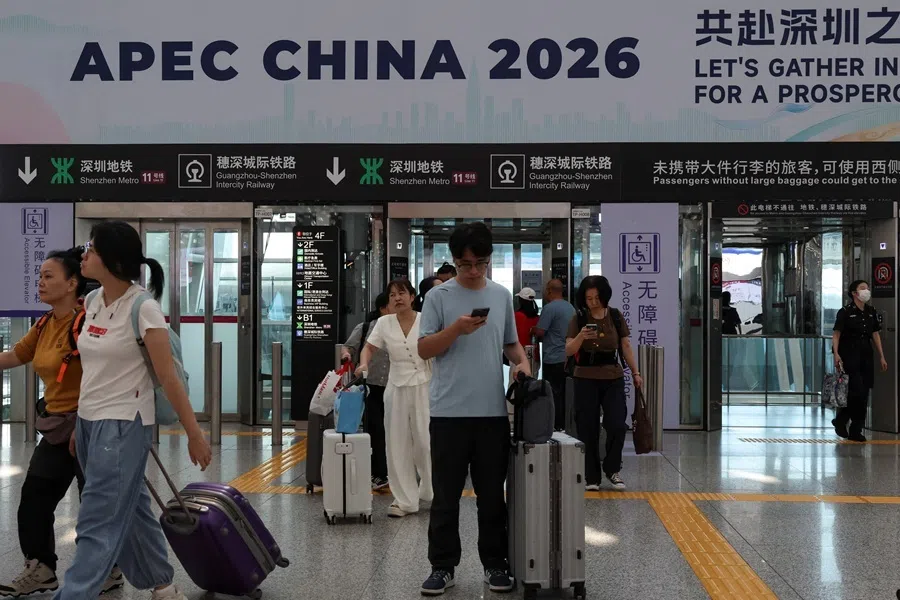 People enter the Shenzhen Bao'an International Airport with their luggage as they walk past a promotion board for the 33rd Asia-Pacific Economic Cooperation (APEC) Economic Leaders' Meeting, in Shenzhen, Guangdong province, China, 28 September 2026.