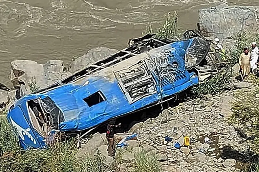 People stand next to a wreck after a bus plunged into a ravine following a bomb attack, which killed 12 people including 9 Chinese workers, in Kohistan district of Khyber Pakhtunkhwa province on 14 July 2021. (AFP)