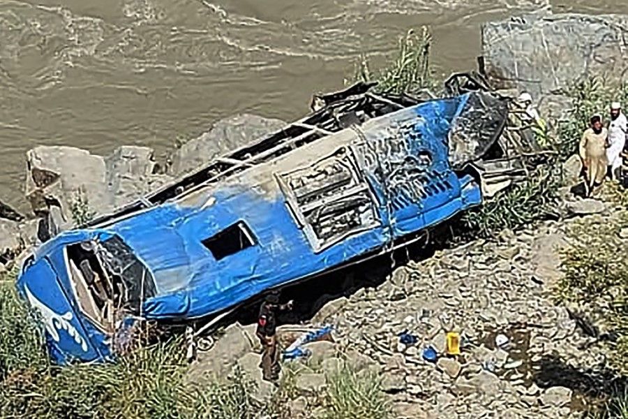 People stand next to a wreck after a bus plunged into a ravine following a bomb attack, which killed 12 people including 9 Chinese workers, in Kohistan district of Khyber Pakhtunkhwa province on 14 July 2021. (AFP)