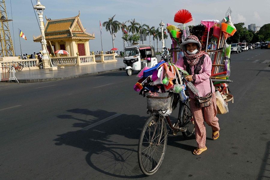 A vendor pushes a bicycle loaded with brushes and brooms for sale along a street in Phnom Penh, Cambodia, on 10 February 2022. (Tang Chhin Sothy/AFP)