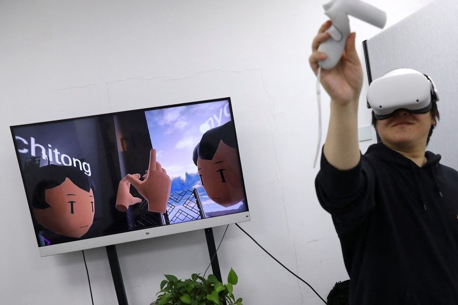 Pan Bohang, founder of vHome, a virtual reality (VR) social gaming platform, wearing Meta's Oculus VR headset uses a touch controller to high-five with a user during a virtual gathering, as a screen shows the virtual content, at an office in Beijing, China, 21 January 2022. (Tingshu Wang/Reuters)